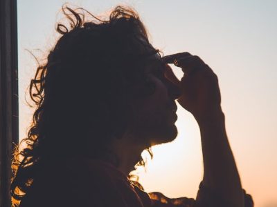 man holding forehead under sunset